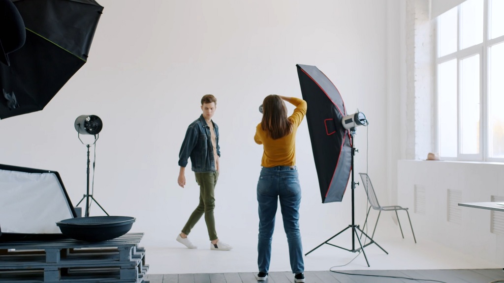 Model pozira ispred fotografa u profesionalnom studiju sa rasvetom i belom pozadinom