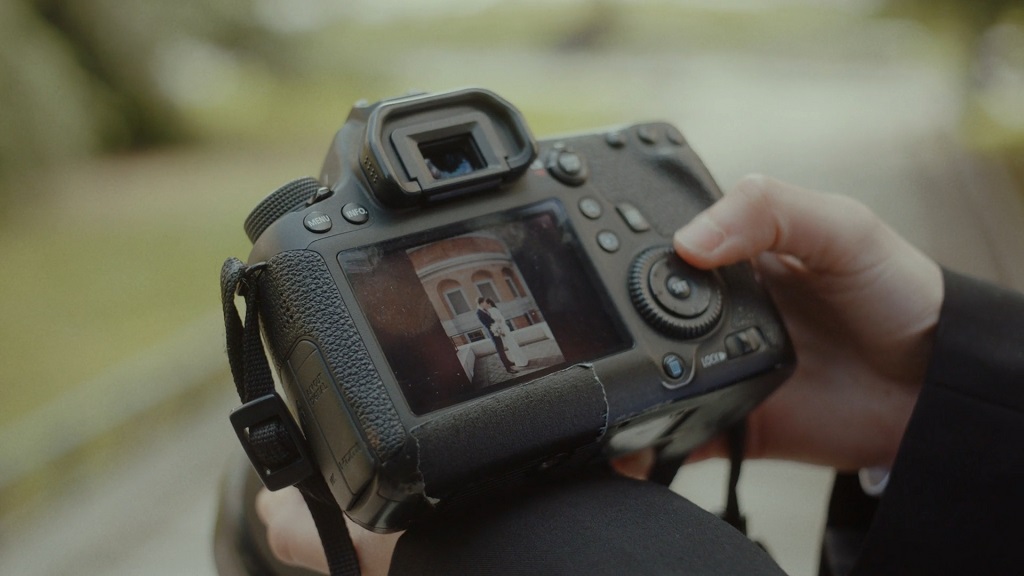 Osoba drži DSLR fotoaparat, na ekranu se prikazuje snimak para ispred zgrade